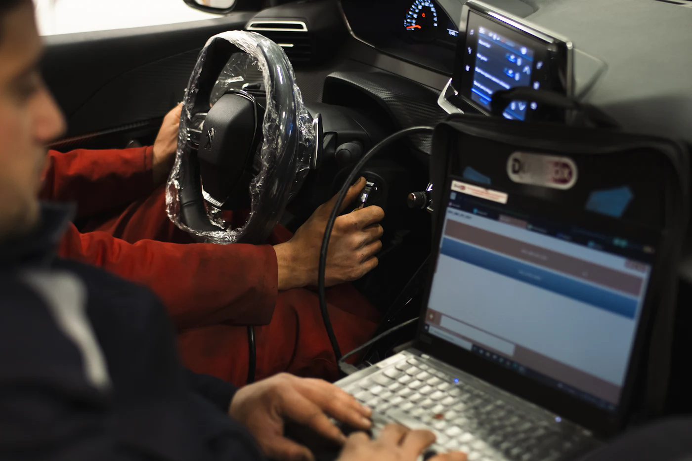 Technician running diagnostics on a laptop connected to a car